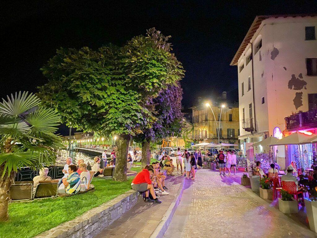 Night view of a lively street with trees, seating, and restaurants.