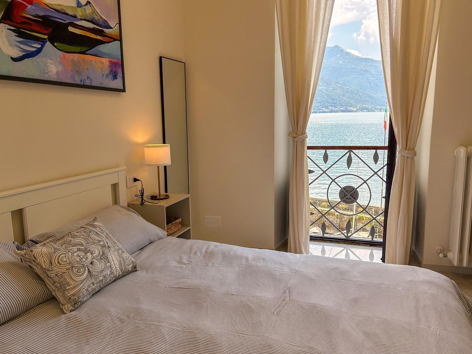 Bedroom with view of lake and mountains. Bed, nightstand, and window with curtains.