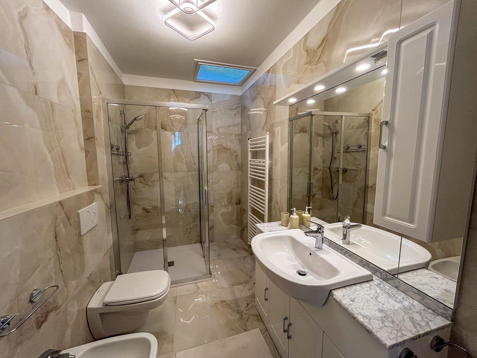 Bathroom with shower, sink, and toilet. Marble tiles and mirror cabinet.