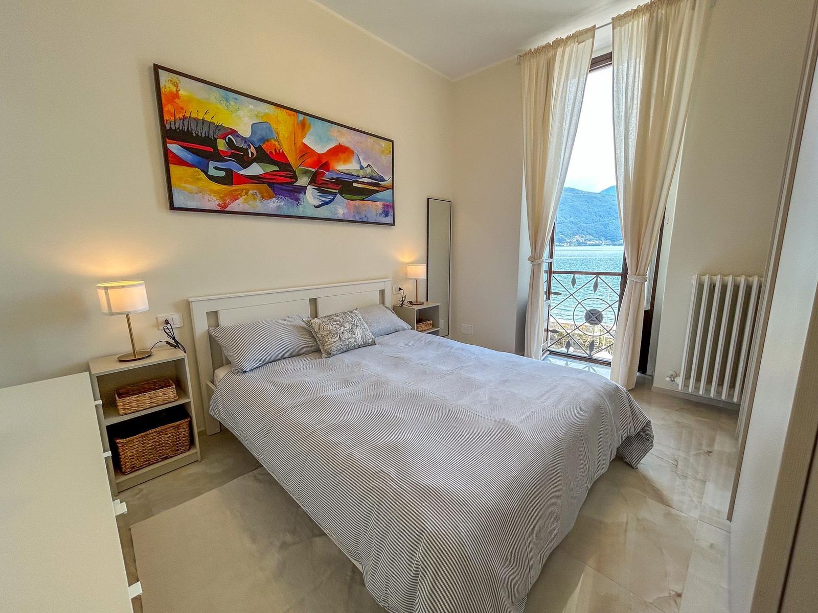 Bedroom with sea and mountain view. Bed, nightstands, wall art, and window.