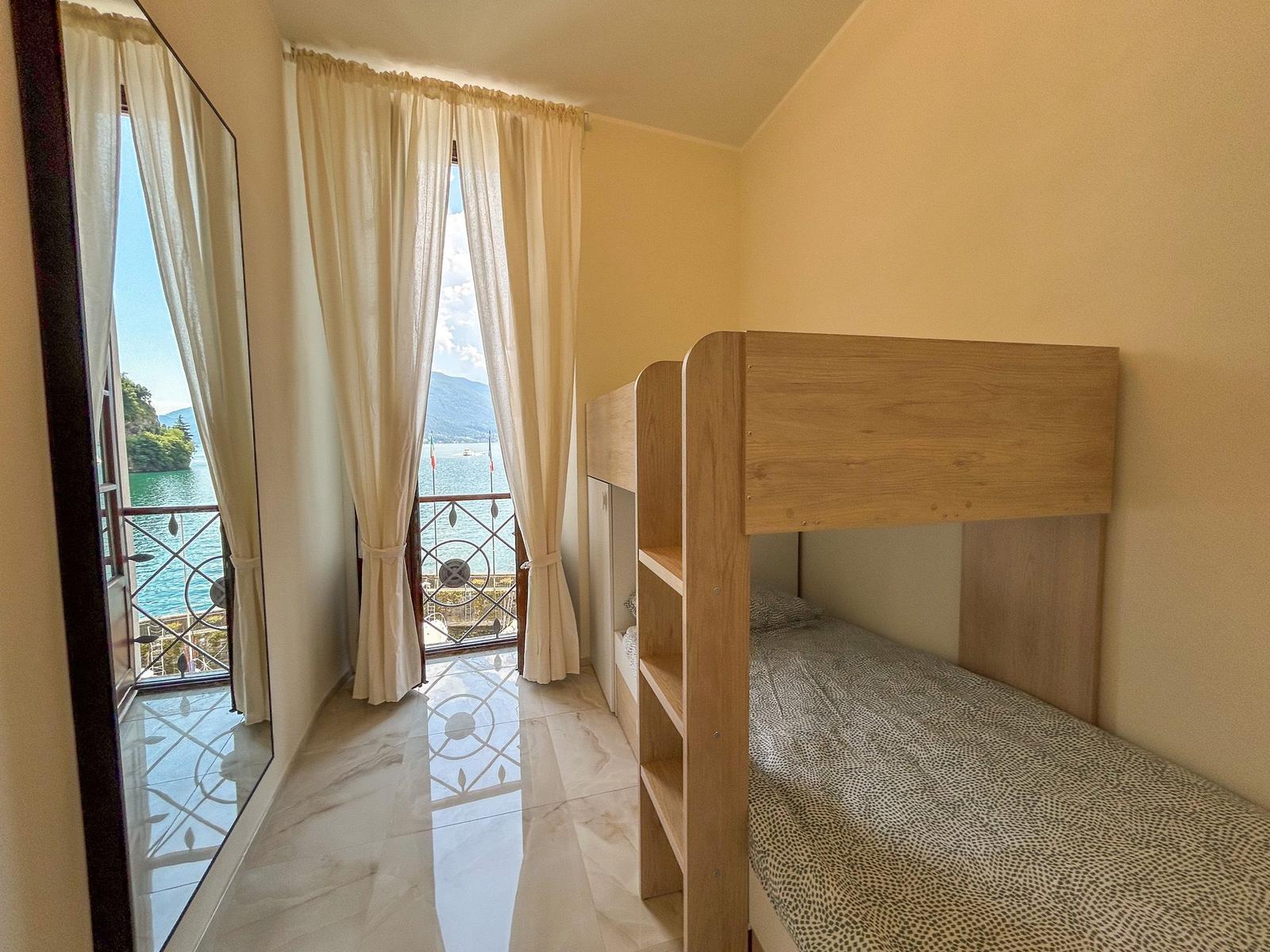 Room with bunk bed and balcony view of lake and mountains.