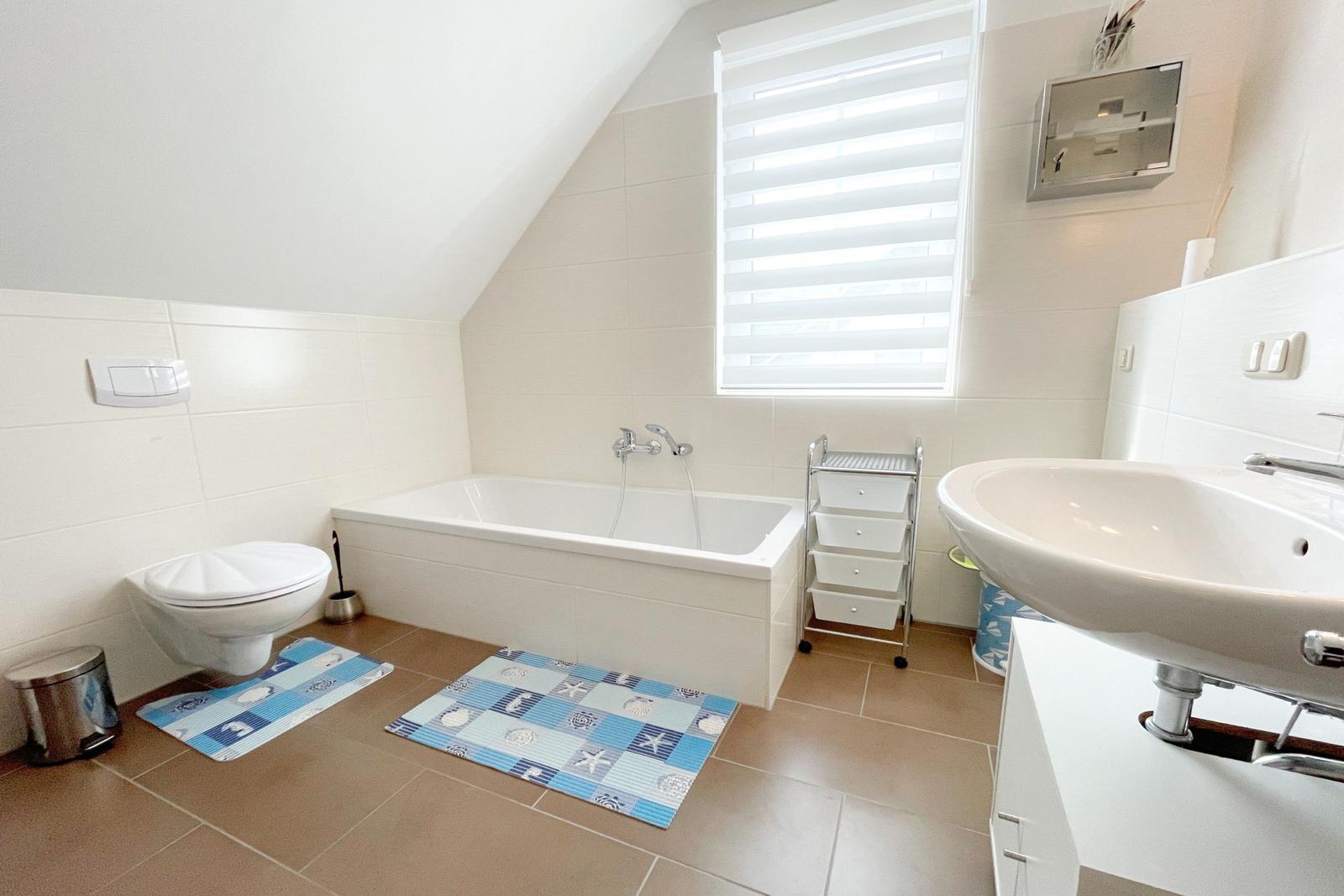 Badezimmer mit Badewanne, Waschbecken und Toilette. Fenster mit Jalousie.