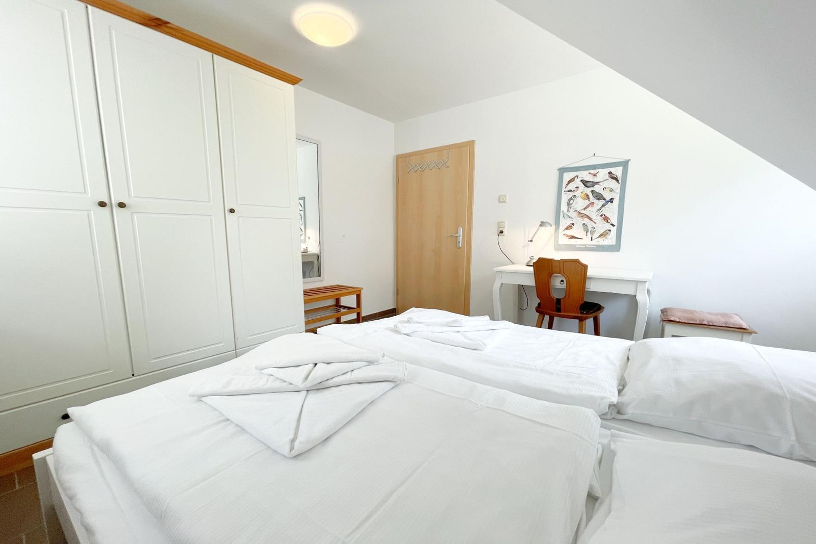 Zimmer mit Doppelbett, Schrank, Schreibtisch und Stuhl. Wandbild mit Vögeln.