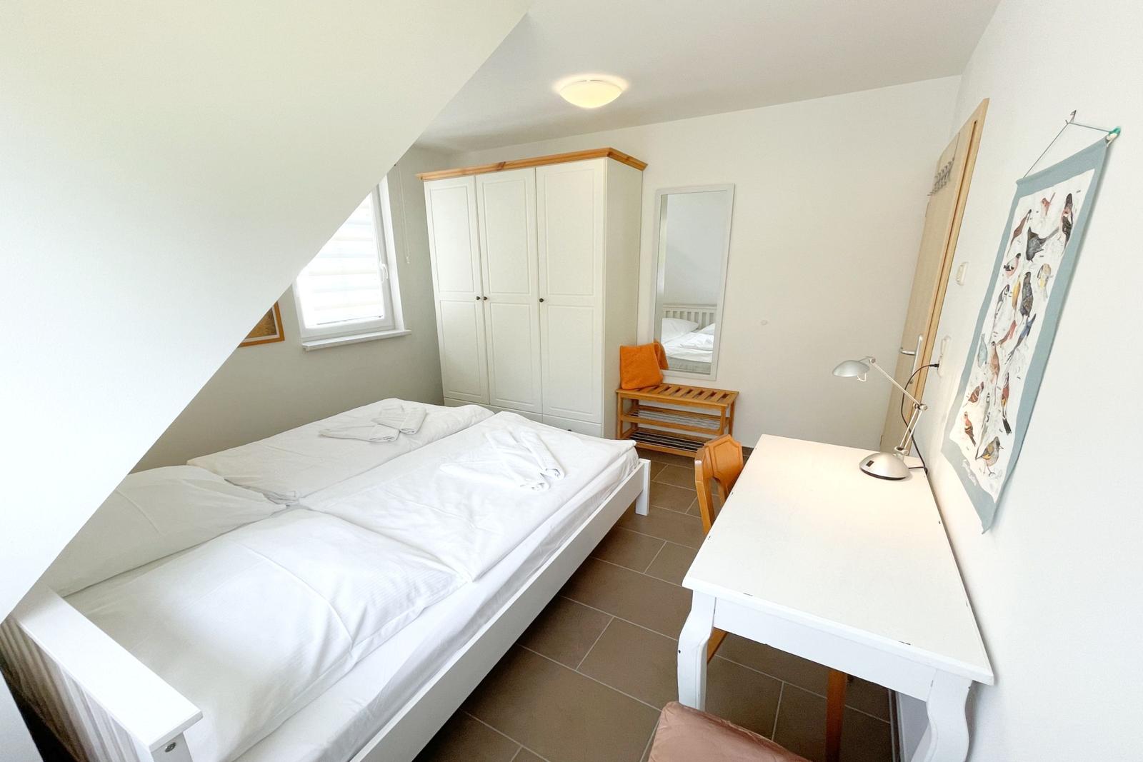 Schlafzimmer mit Doppelbett, Schrank, Spiegel und Schreibtisch.