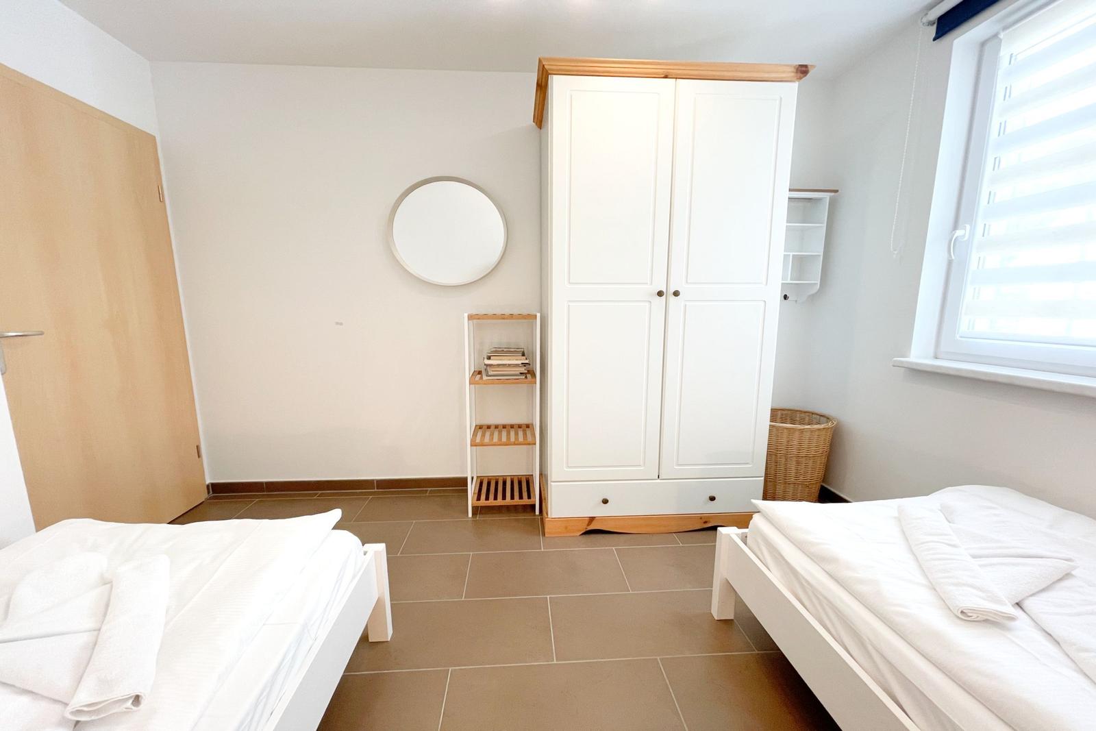 Zwei Betten, weißer Schrank und runder Spiegel im Zimmer.