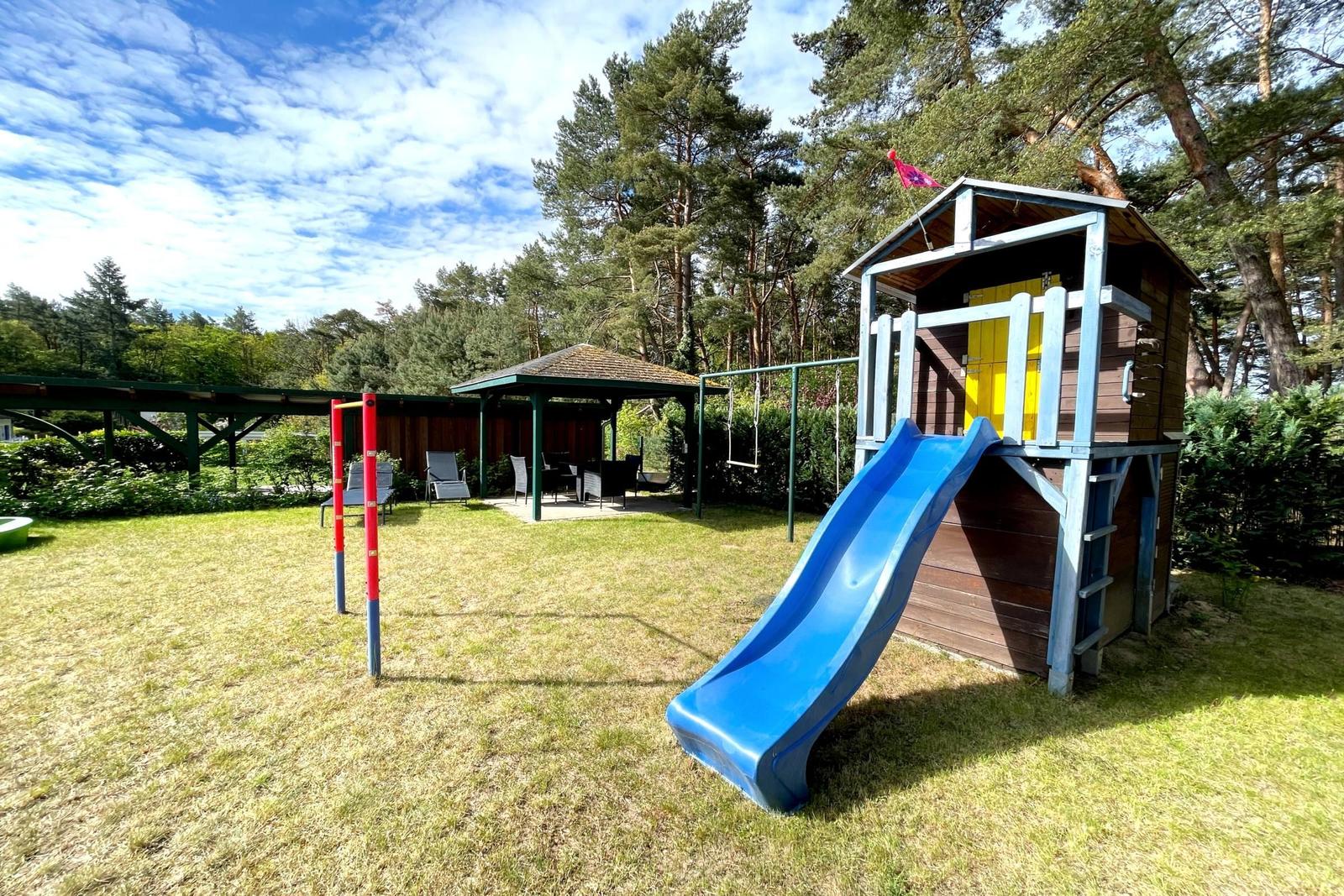 Hinterhof mit Spielhaus, Rutsche und Grillplatz unter Bäumen.