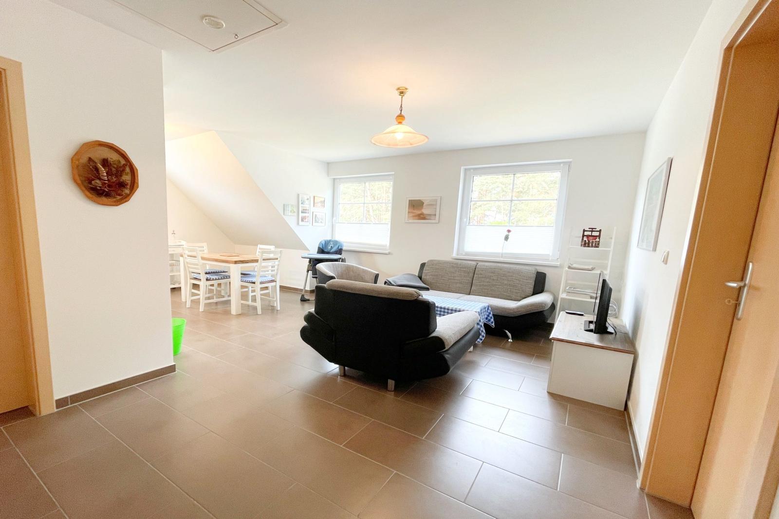 Wohn- und Essbereich mit Sofa, Stühlen und Fenstern. Holzboden und Deckenleuchte.