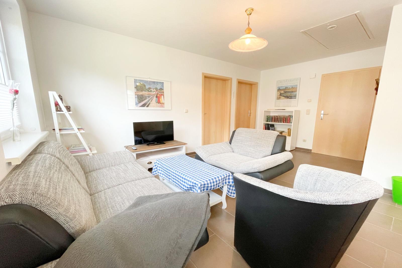 Wohnzimmer mit Sofa, Sessel und Fernseher. Tisch mit kariertem Tuch.