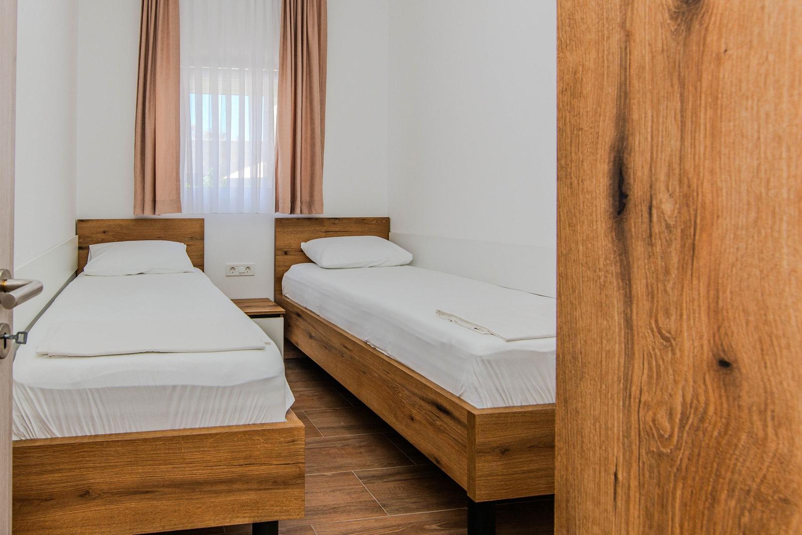 Zwei Einzelbetten mit Holzgestell und weißer Bettwäsche unter einem Fenster mit Vorhängen.