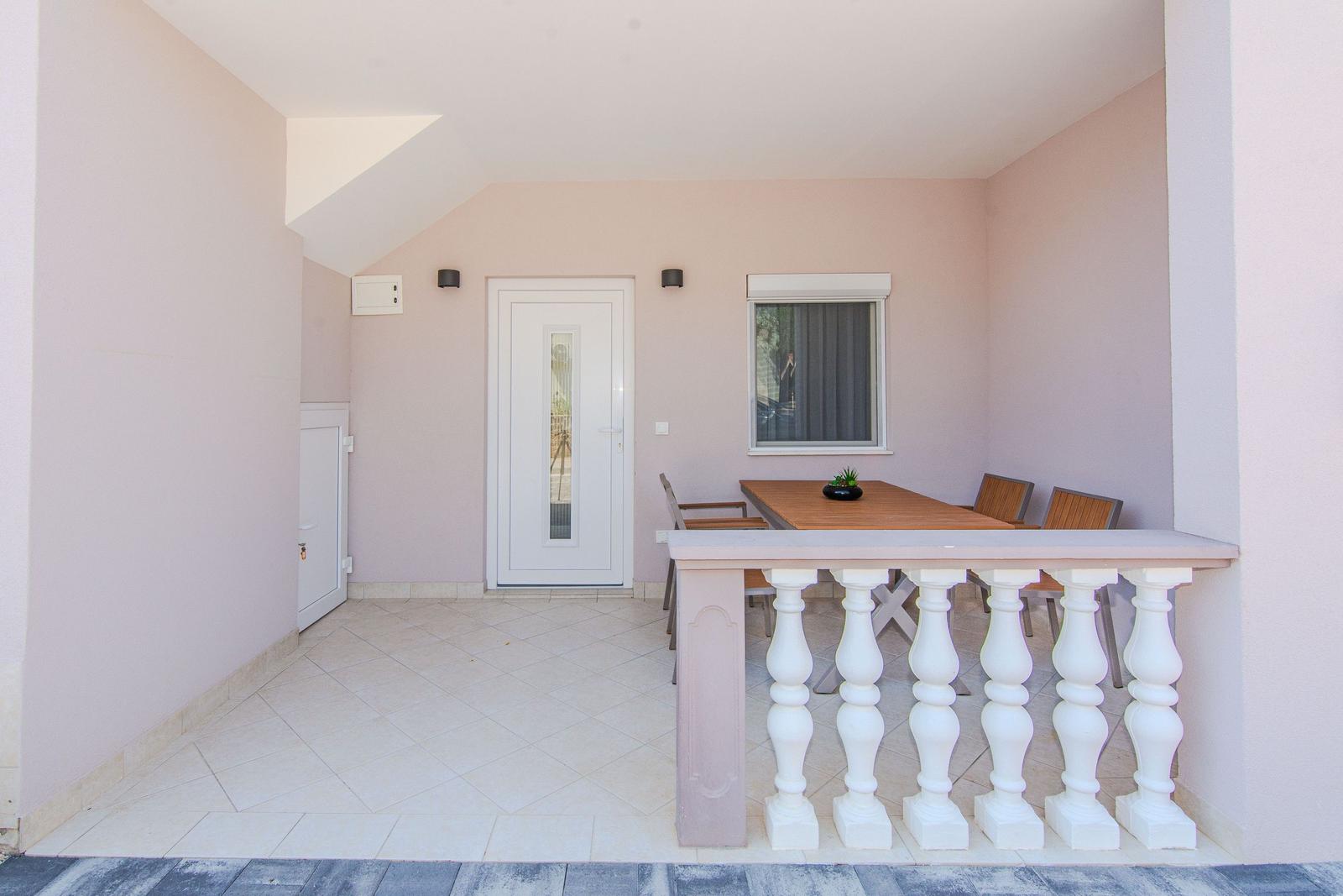 Terrasse mit Tisch, Stühlen und weißer Balustrade. Hintergrund: Tür und Fenster.