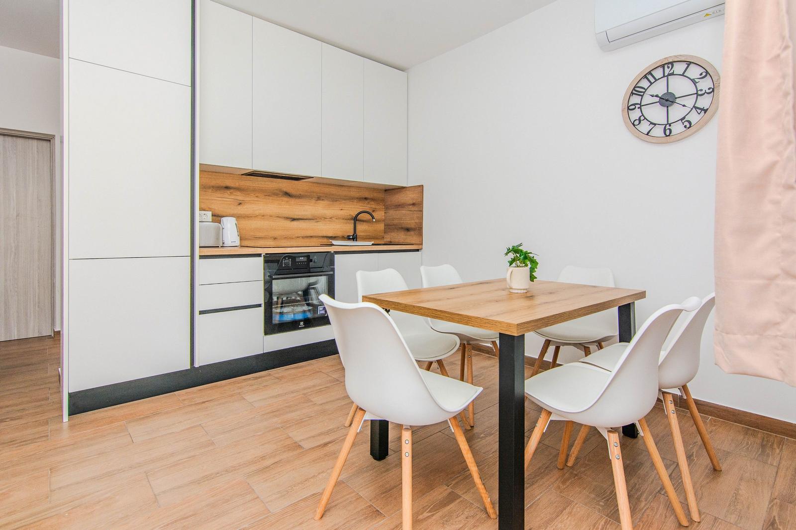 Küche mit Esstisch und Stühlen. Holz- und Weißtöne dominieren.