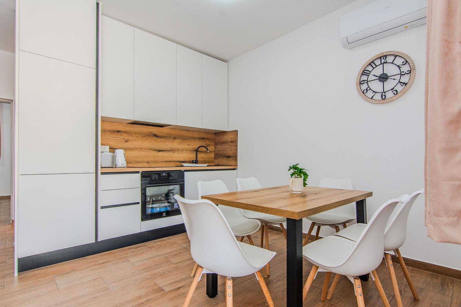 Küche mit Esstisch und Stühlen. Wanduhr und Klimaanlage sichtbar.