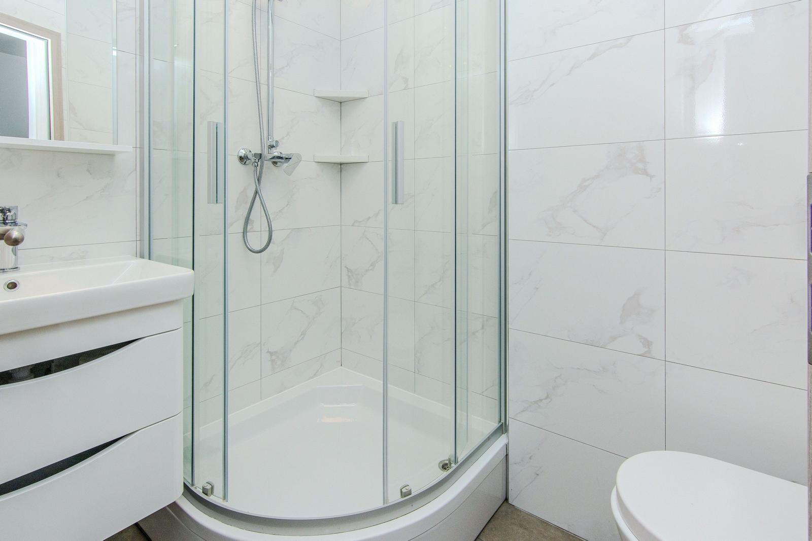 Badezimmer mit Dusche, Waschbecken und Toilette. Fliesen und Möbel sind weiß.