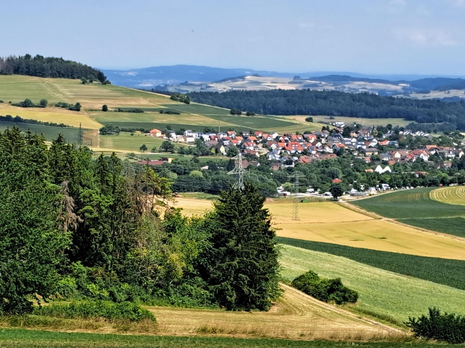 Panorama über eine ländliche Gegend mit Feldern, Wäldern und einem Dorf.