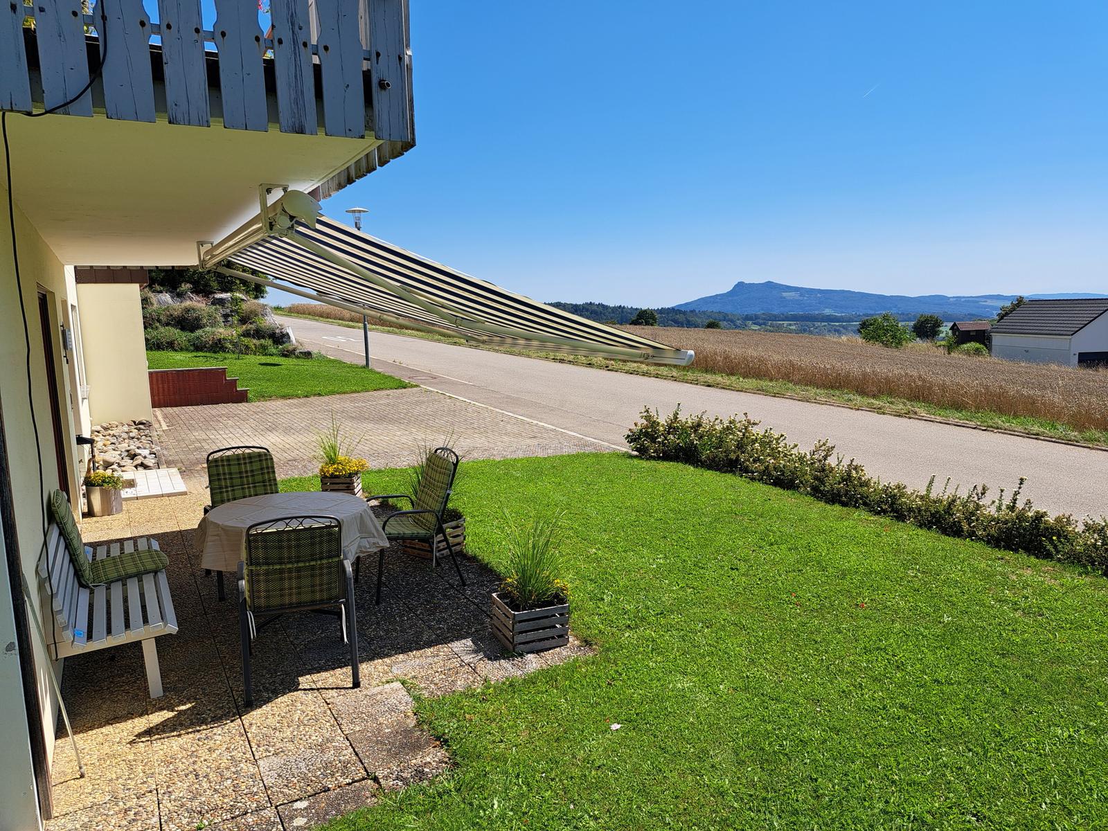 Terrasse mit Tisch, Stühlen und Blick auf Felder und Berge.