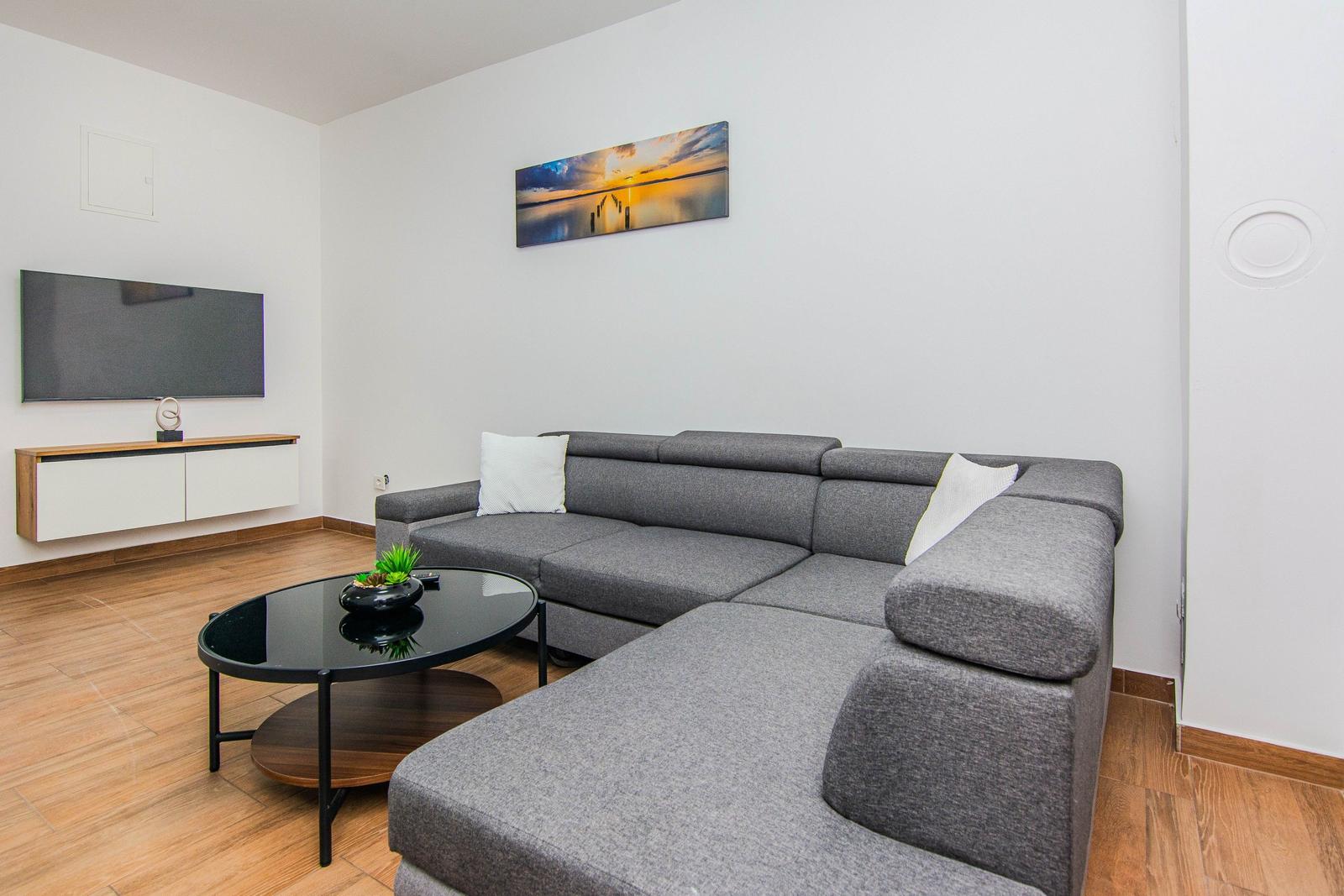 Wohnzimmer mit grauem Sofa, Fernseher und Tisch