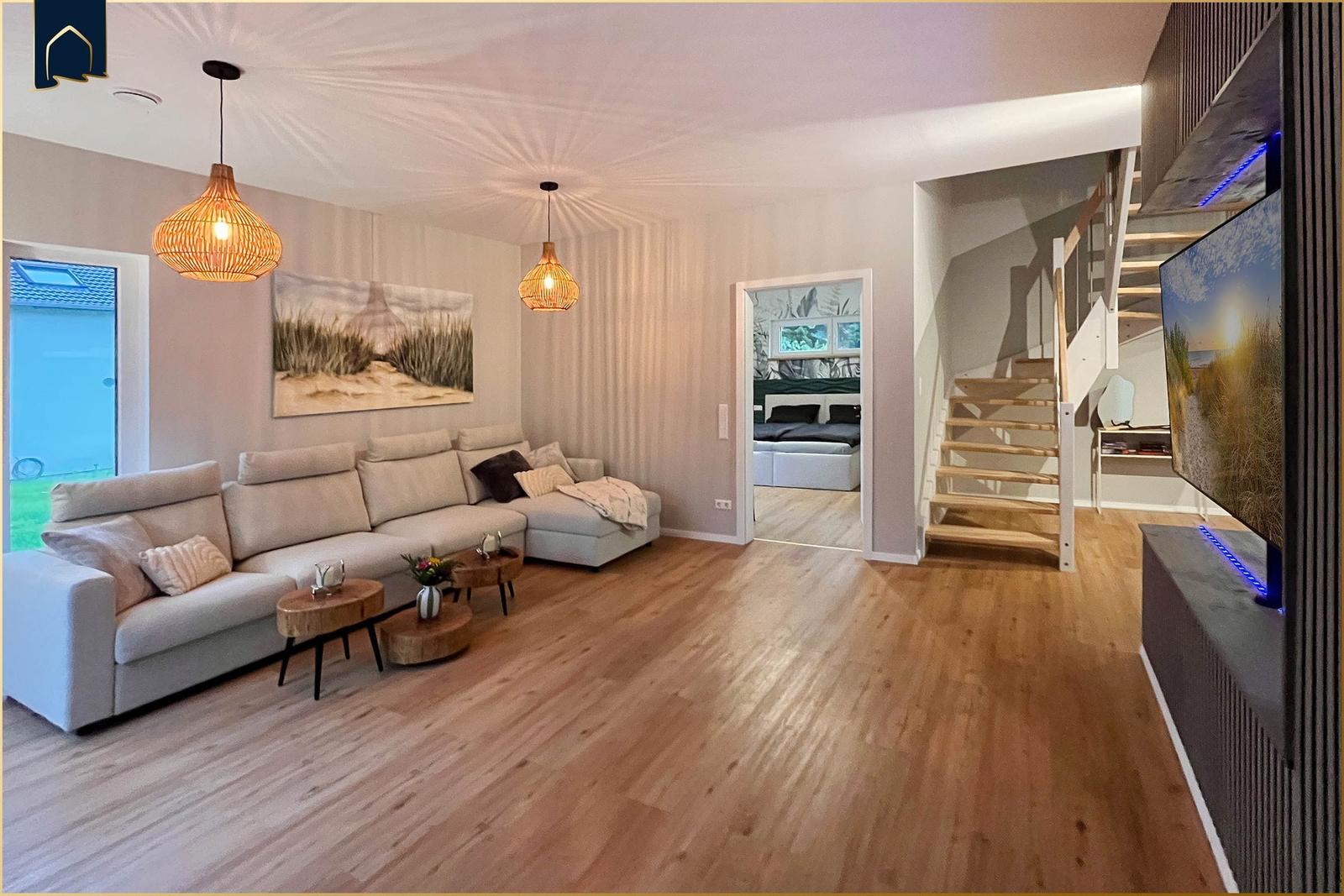 Wohnzimmer mit Sofa, Treppenhaus und TV. Durchgang zum Schlafzimmer.