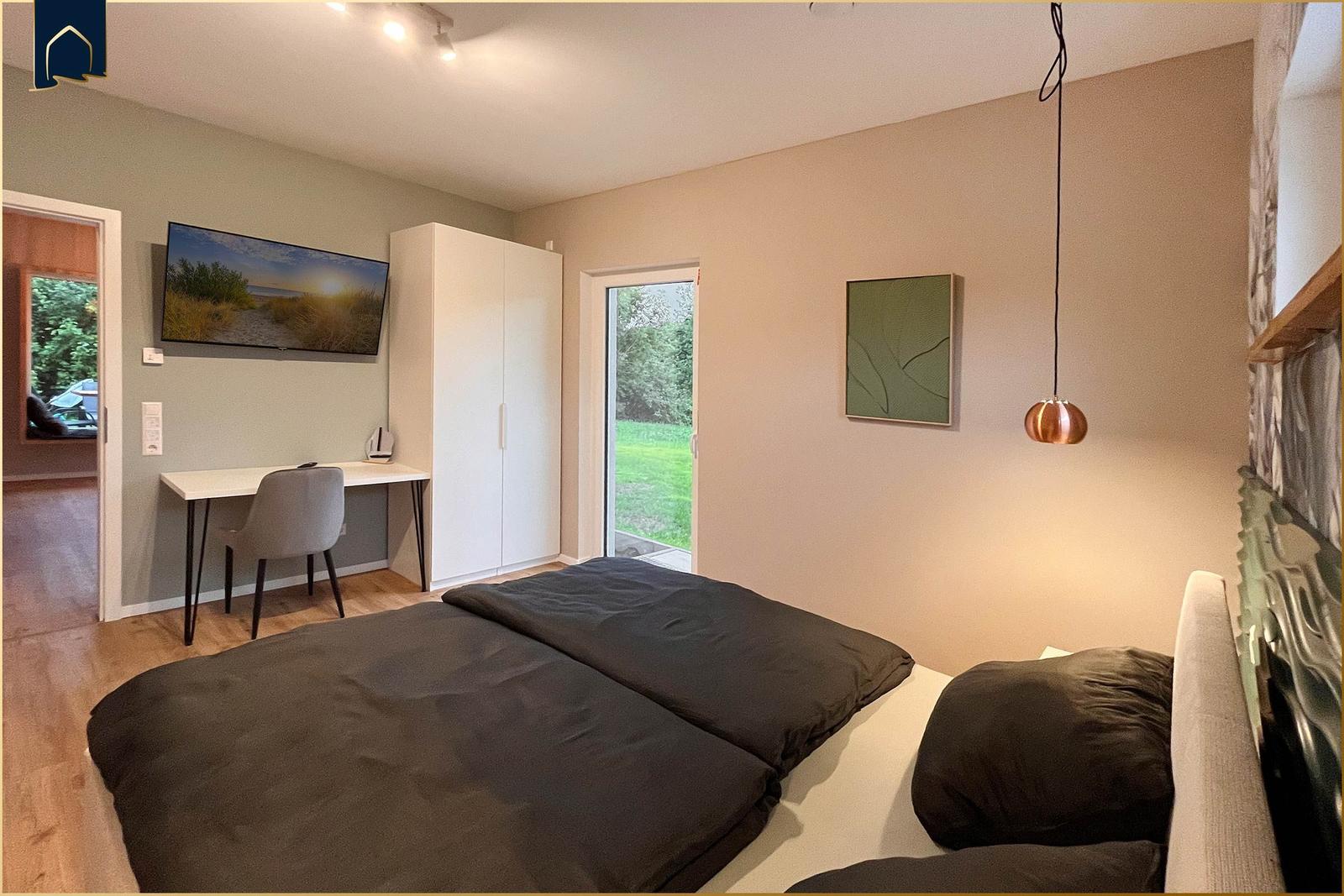 Schlafzimmer mit Bett, Schreibtisch, Kleiderschrank und Zugang zum Garten.