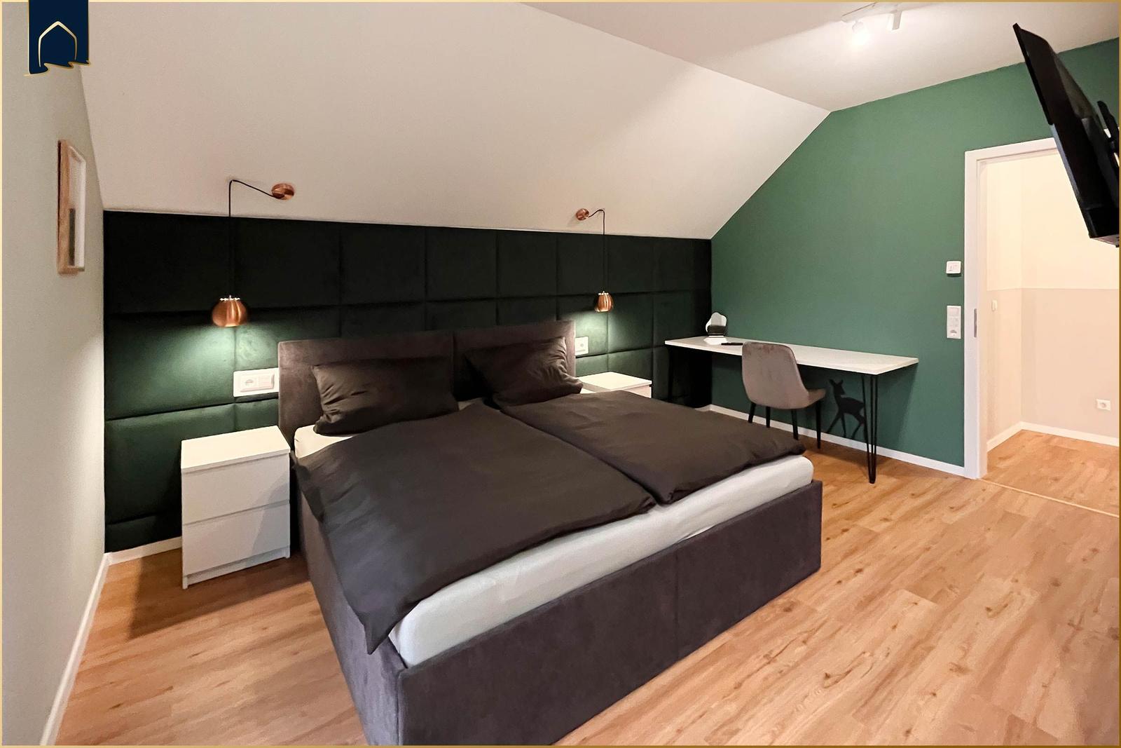 Schlafzimmer mit Doppelbett, Schreibtisch und Fernseher an der Wand.