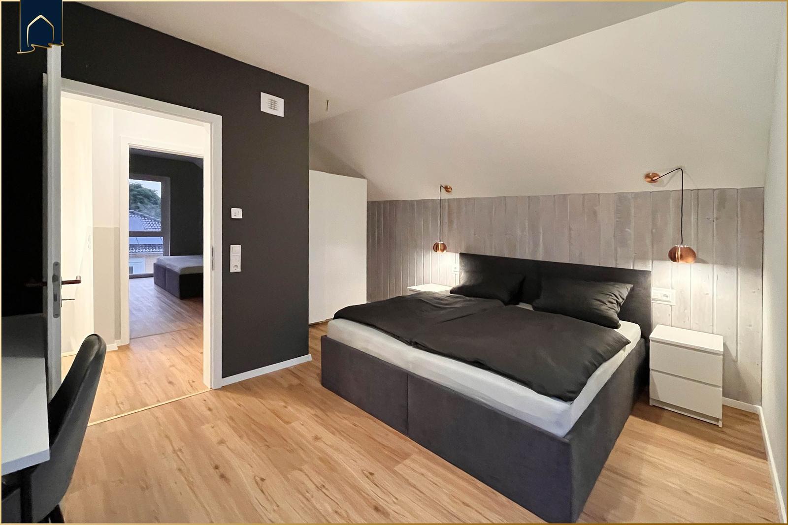 Schlafzimmer mit Doppelbett, Holzboden und Nachttischen. Durchgang zu Wohnbereich.