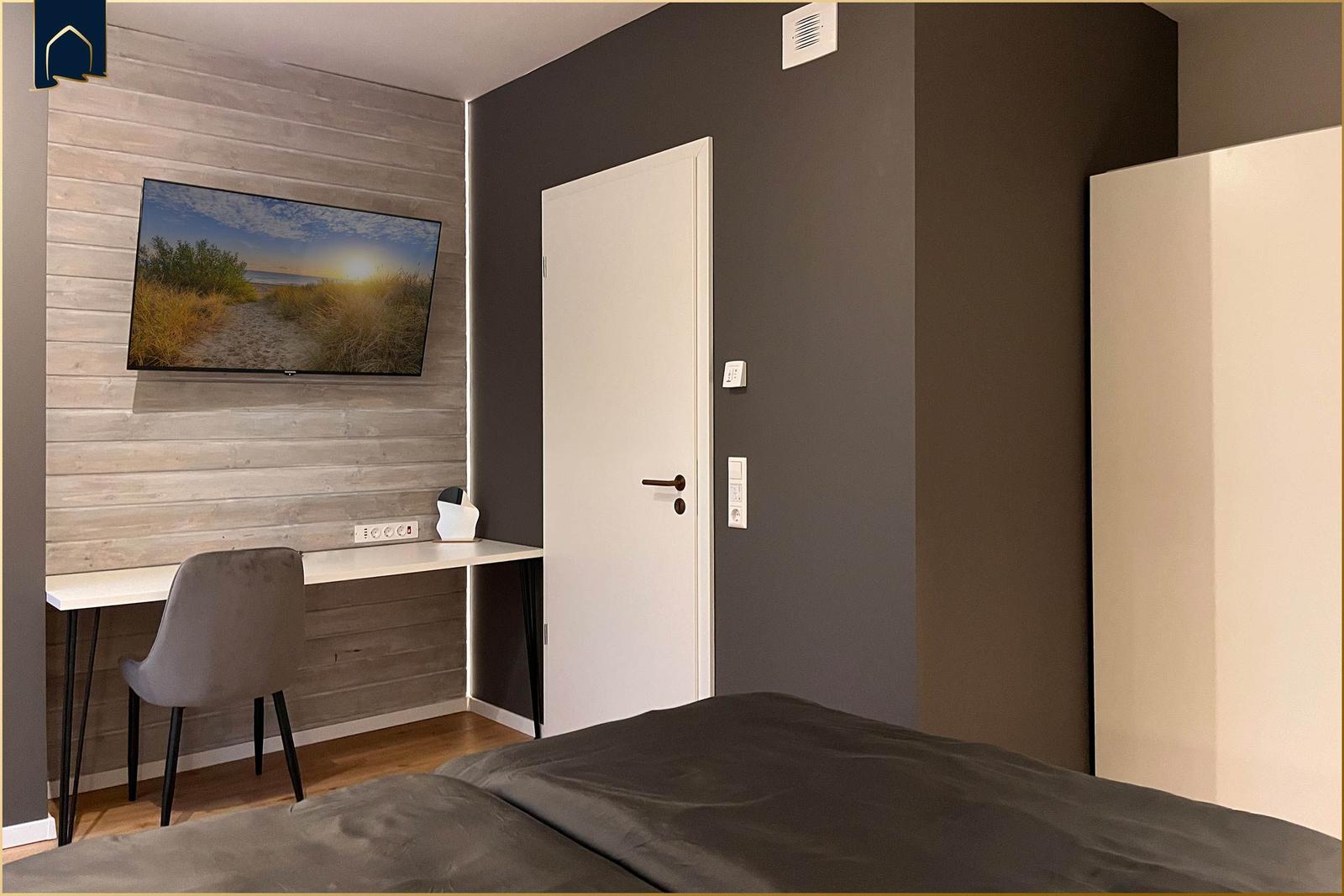 Schlafzimmer mit Bett, Schreibtisch und Wandbild. Tür und Kleiderschrank sichtbar.