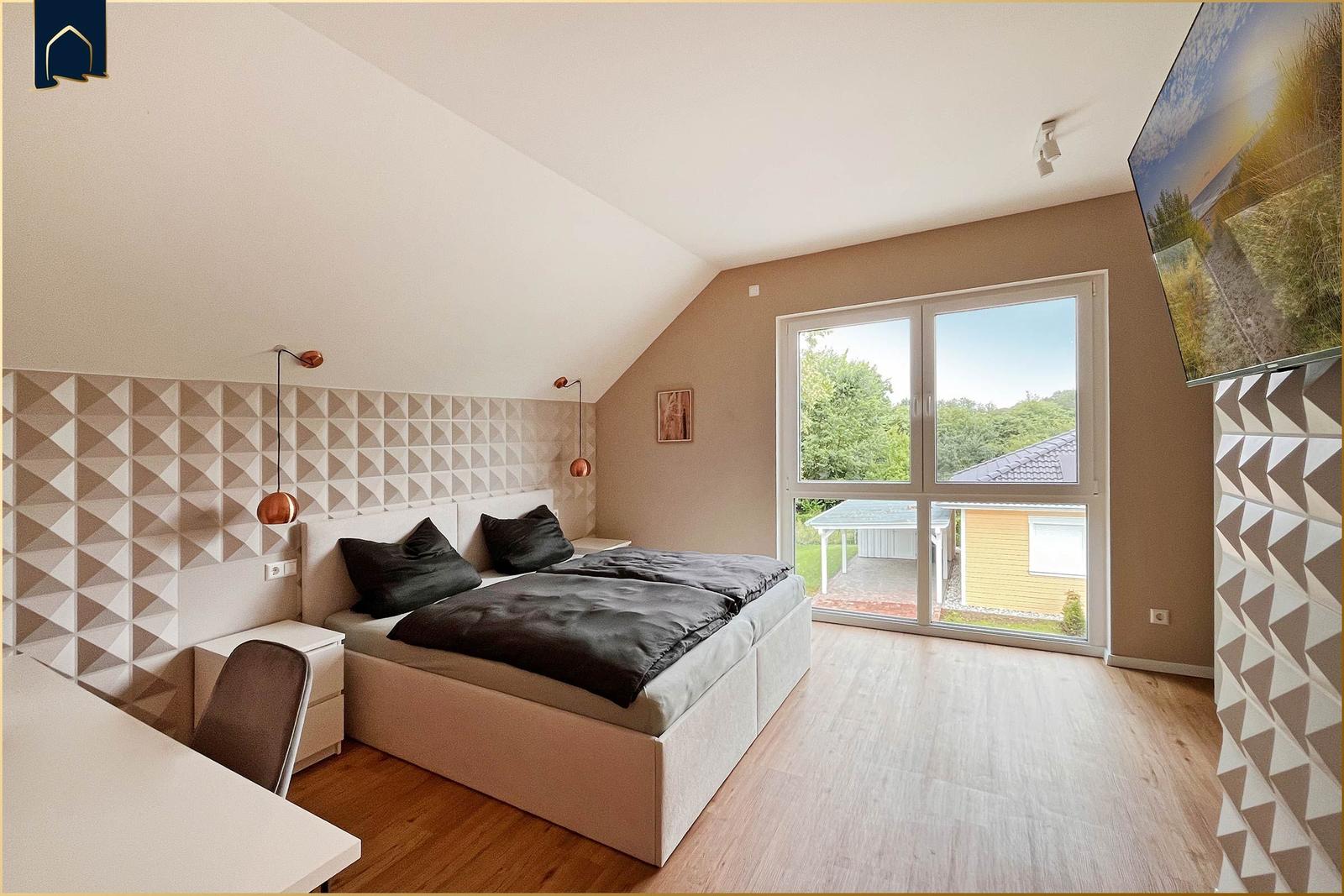 Schlafzimmer mit Doppelbett, Schreibtisch und großem Fenster zur Außensicht.