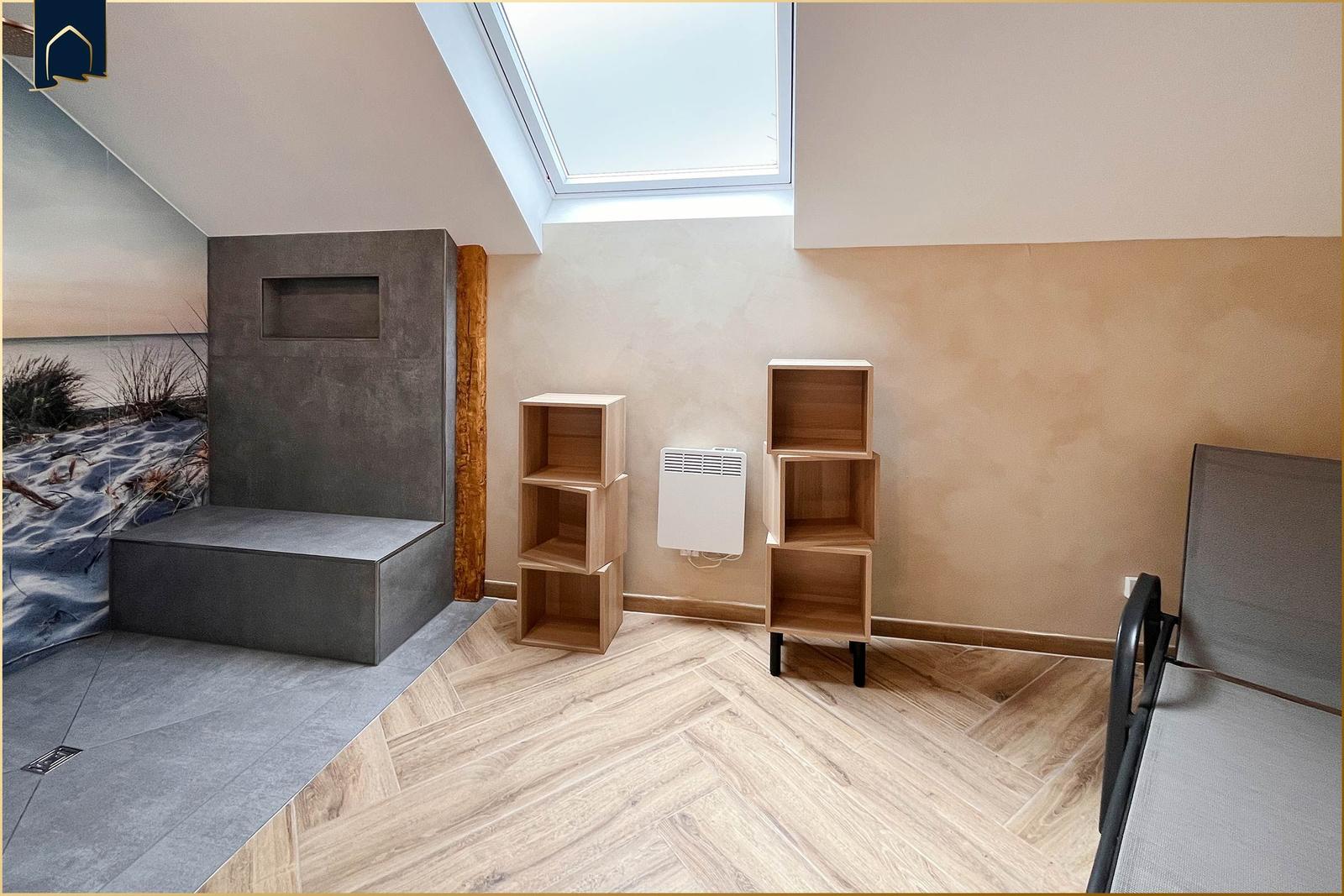 Raum mit Holzboden, Bücherregalen und Dachfenster. Wandbild und Betonbank sichtbar.