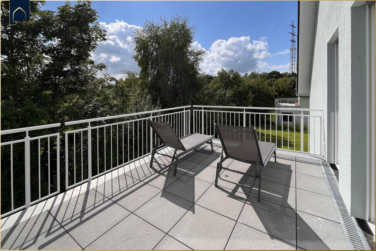Terrasse mit zwei Liegestühlen und Blick auf grüne Bäume.