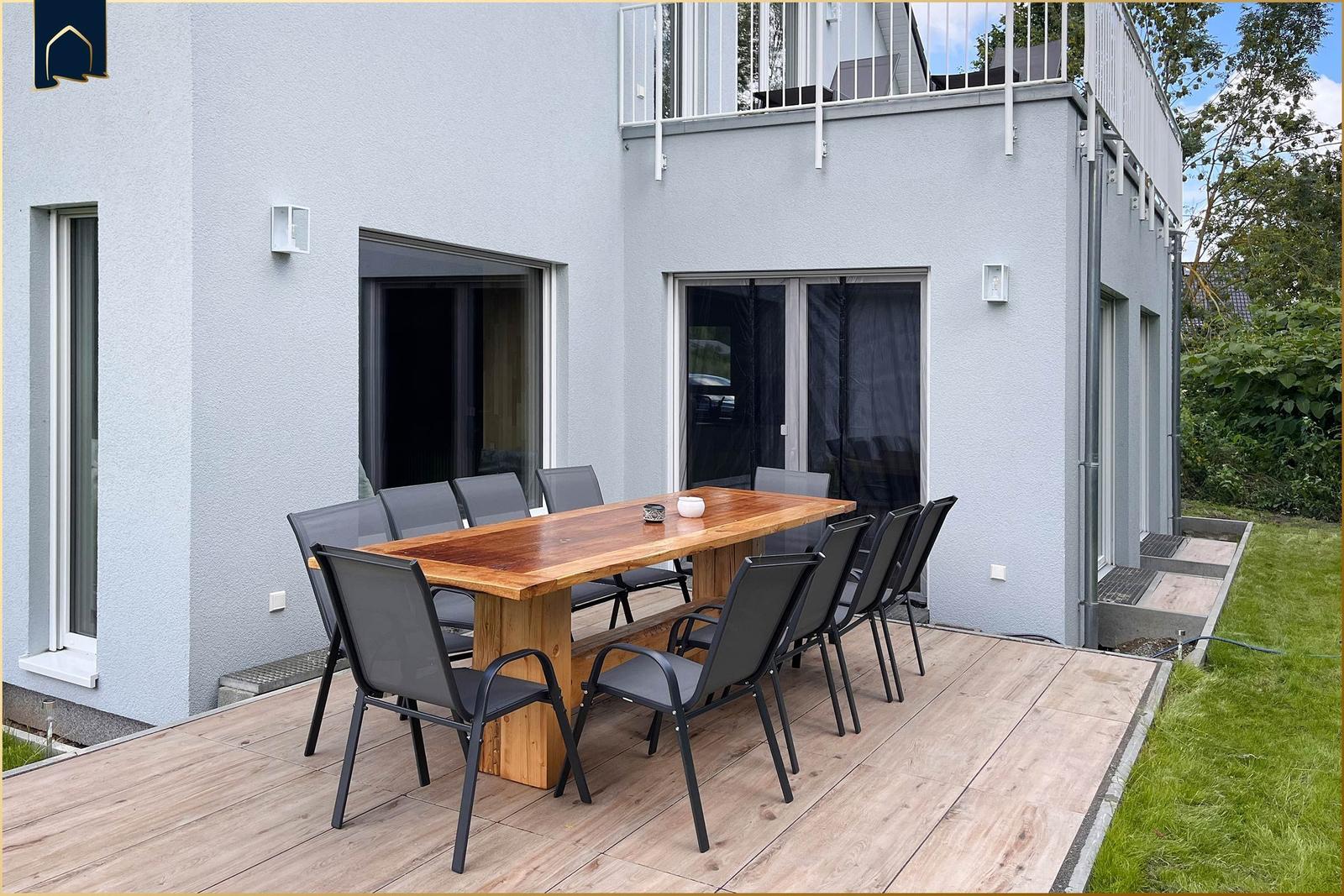 Terrasse mit Holztisch und acht Stühlen vor modernem Haus