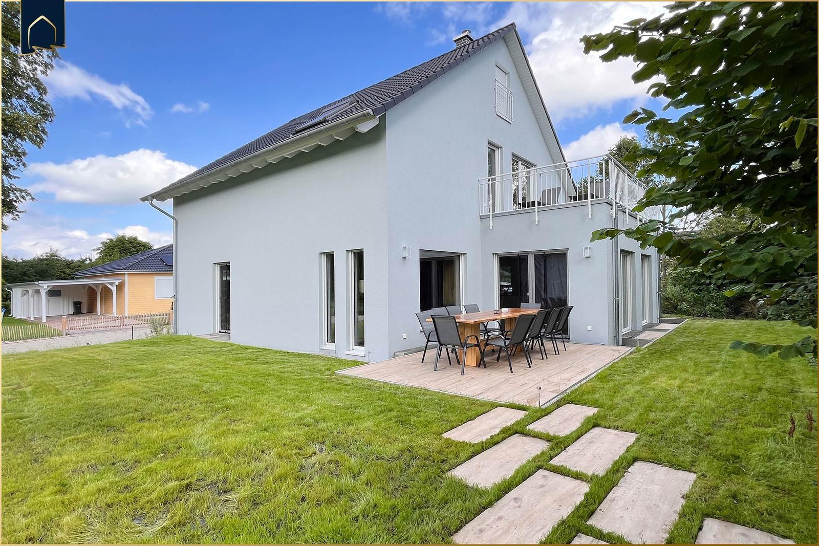 Moderne Villa mit Terrasse, Garten und Balkon. Holztisch mit Stühlen im Freien.
