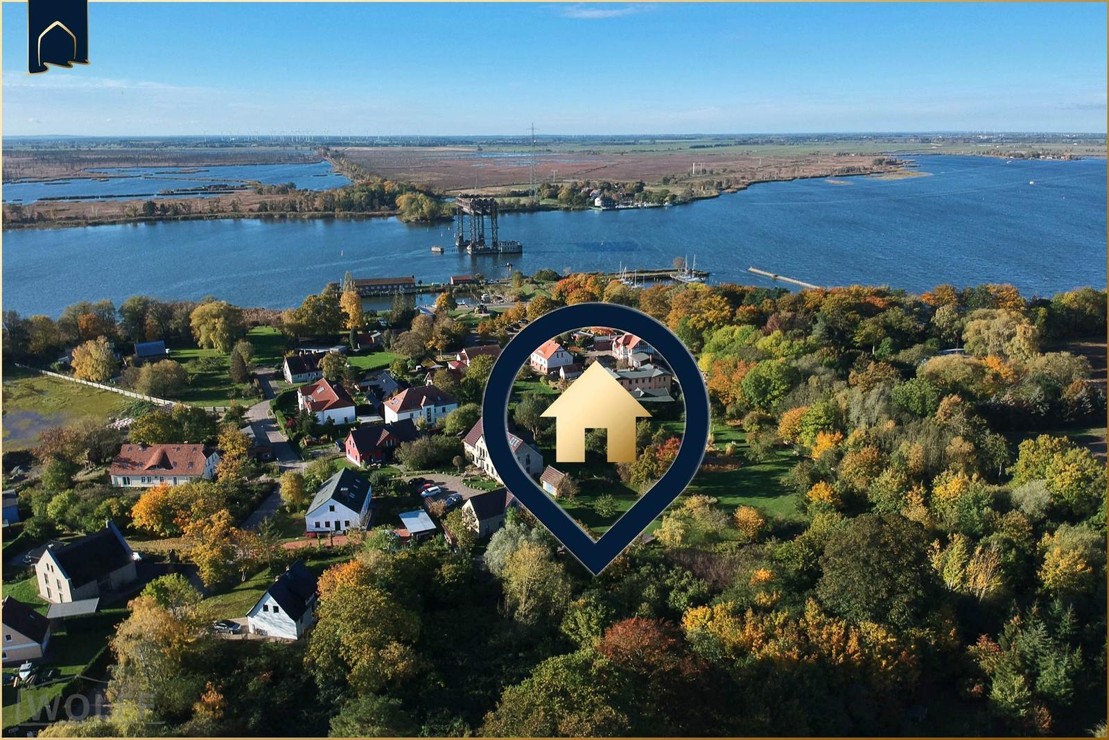 Aerial view of a village near a large water body with autumn trees.