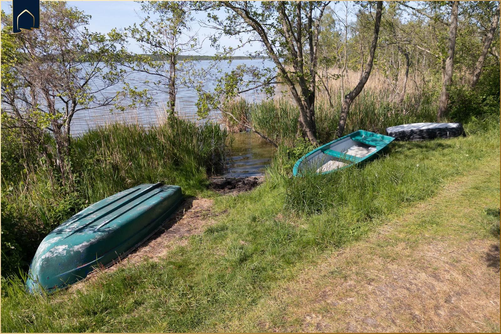 Zwei grüne Boote liegen am Ufer eines Sees unter Bäumen.