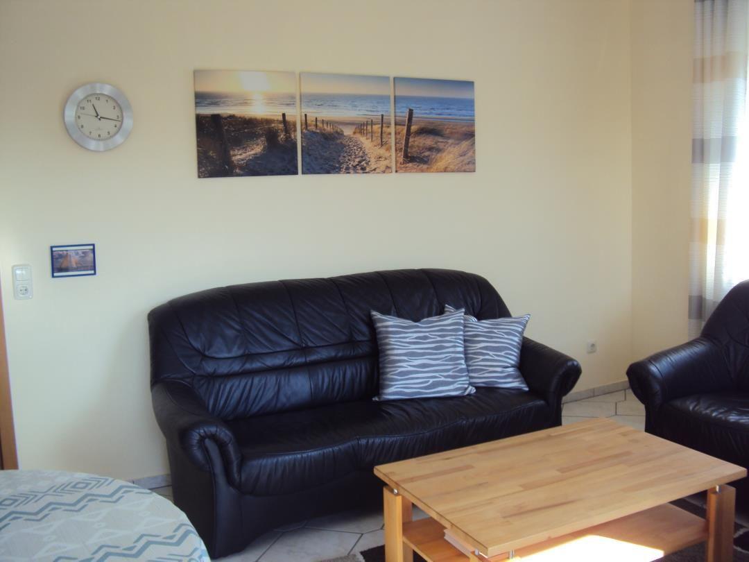 Schwarzes Ledersofa mit Kissen, Holztisch und Wandbild mit Strandmotiv.