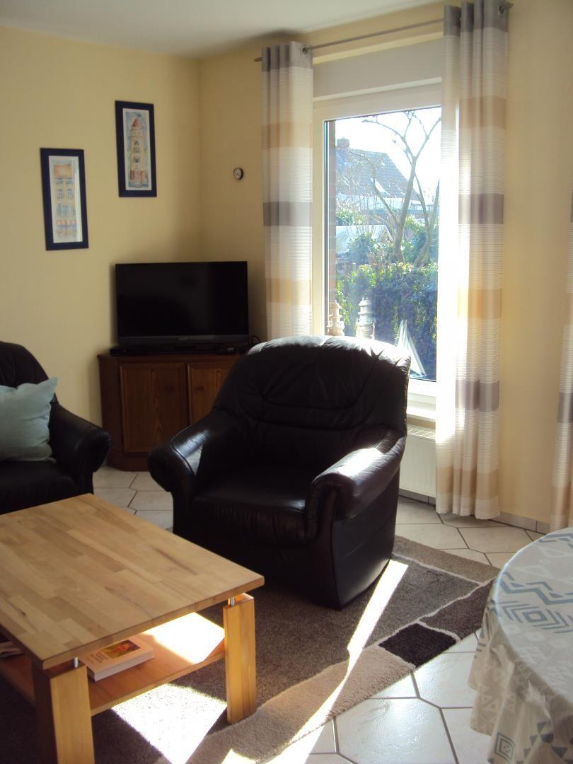 Wohnzimmer mit Sofa, Fernseher und großem Fenster mit Blick auf Garten.