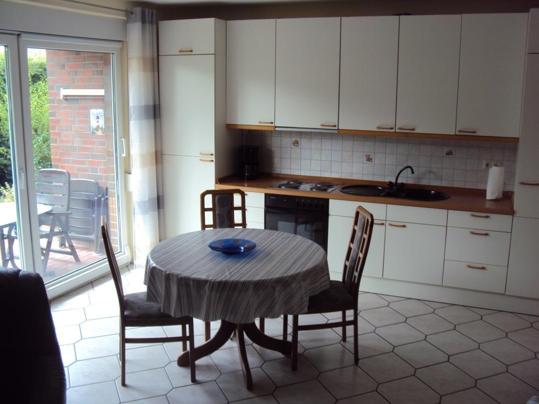 Küche mit Esstisch, Fenster zum Balkon und weißen Schränken.