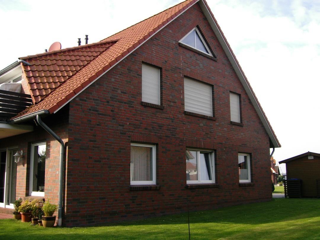 Rotes Ziegelhaus mit Dachgaube und Gartenterrasse.