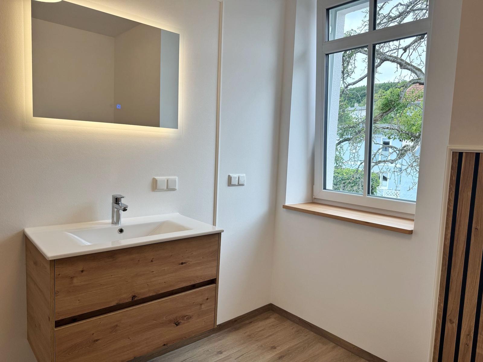 Badezimmer mit Waschbecken, Spiegel und Fenster mit Blick.