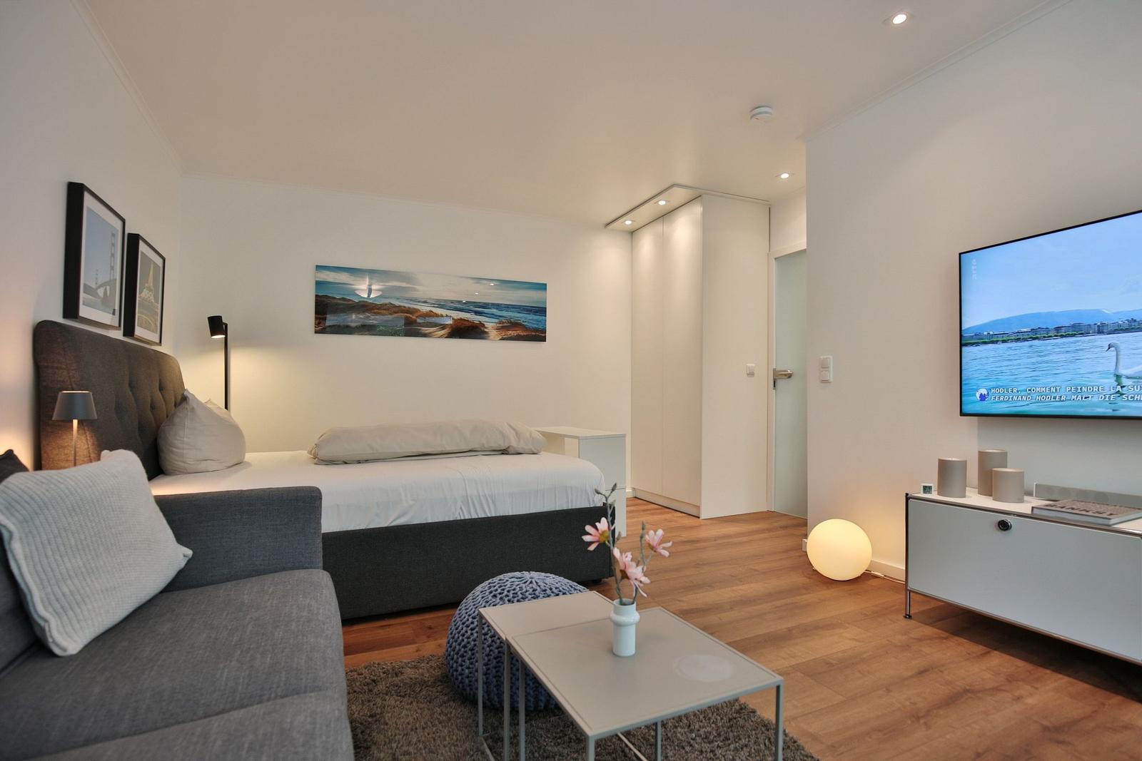 Schlafzimmer mit Bett, Sofa, Fernseher und Holzboden.