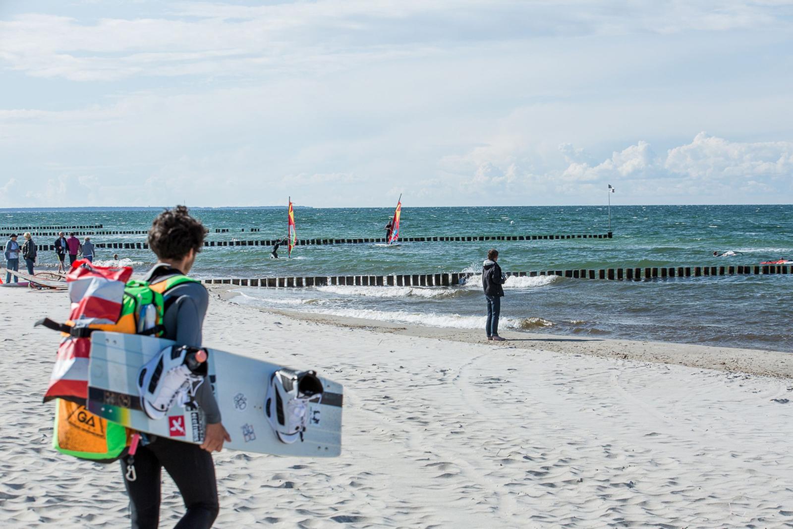 Sandy Strand mit Windsurfern und Wellen im Hintergrund.