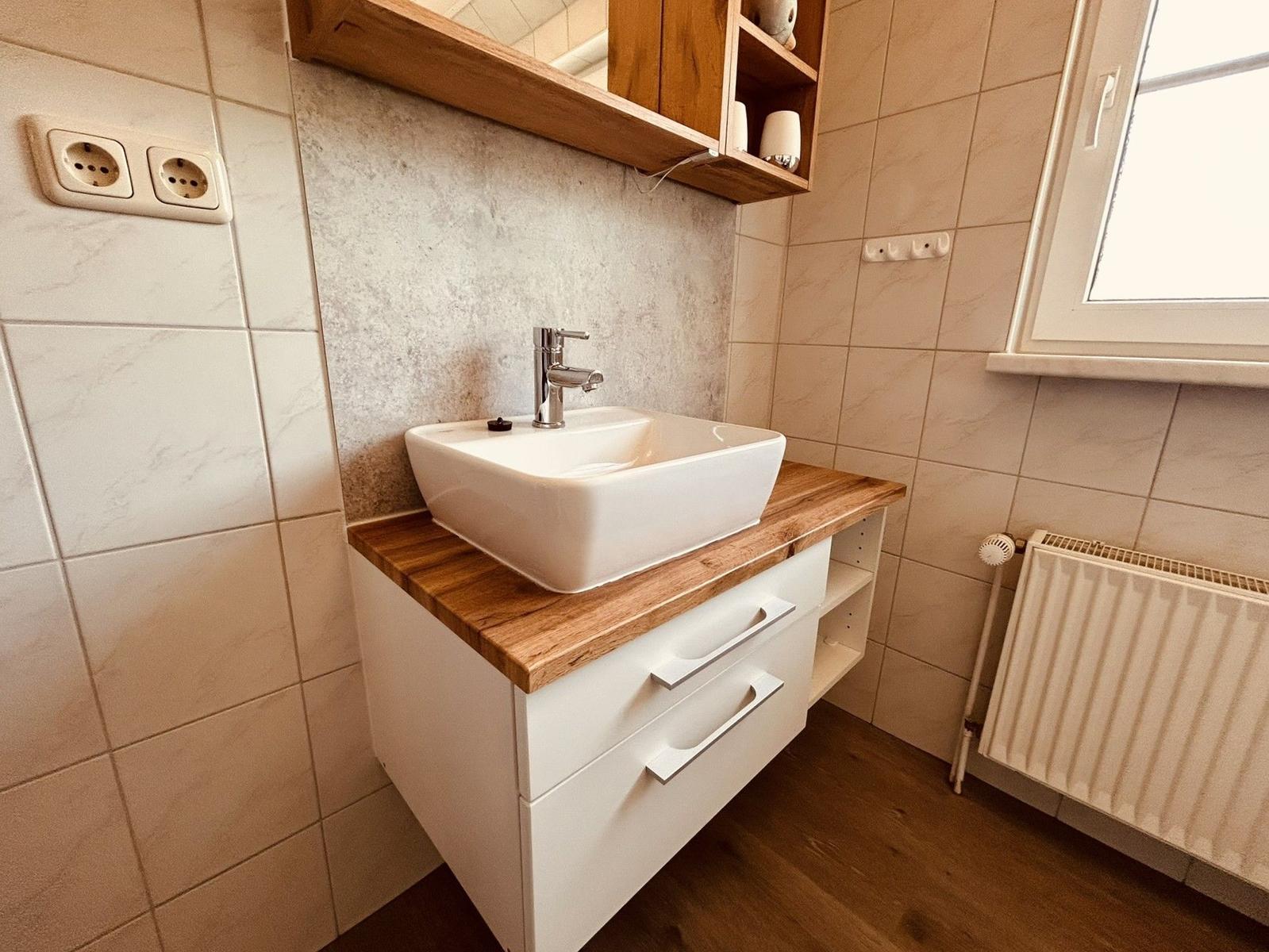 Bad mit Waschbecken, Holzoberfläche und Wandregal.