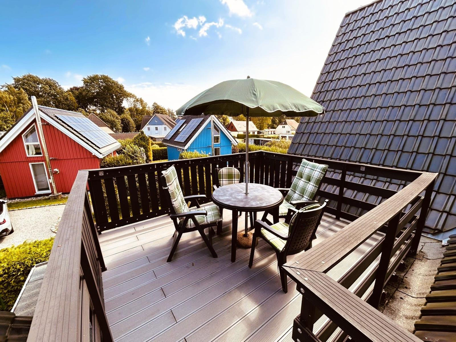 Terrasse mit Tisch, Stühlen und Sonnenschirm. Blick auf rote und blaue Häuser.