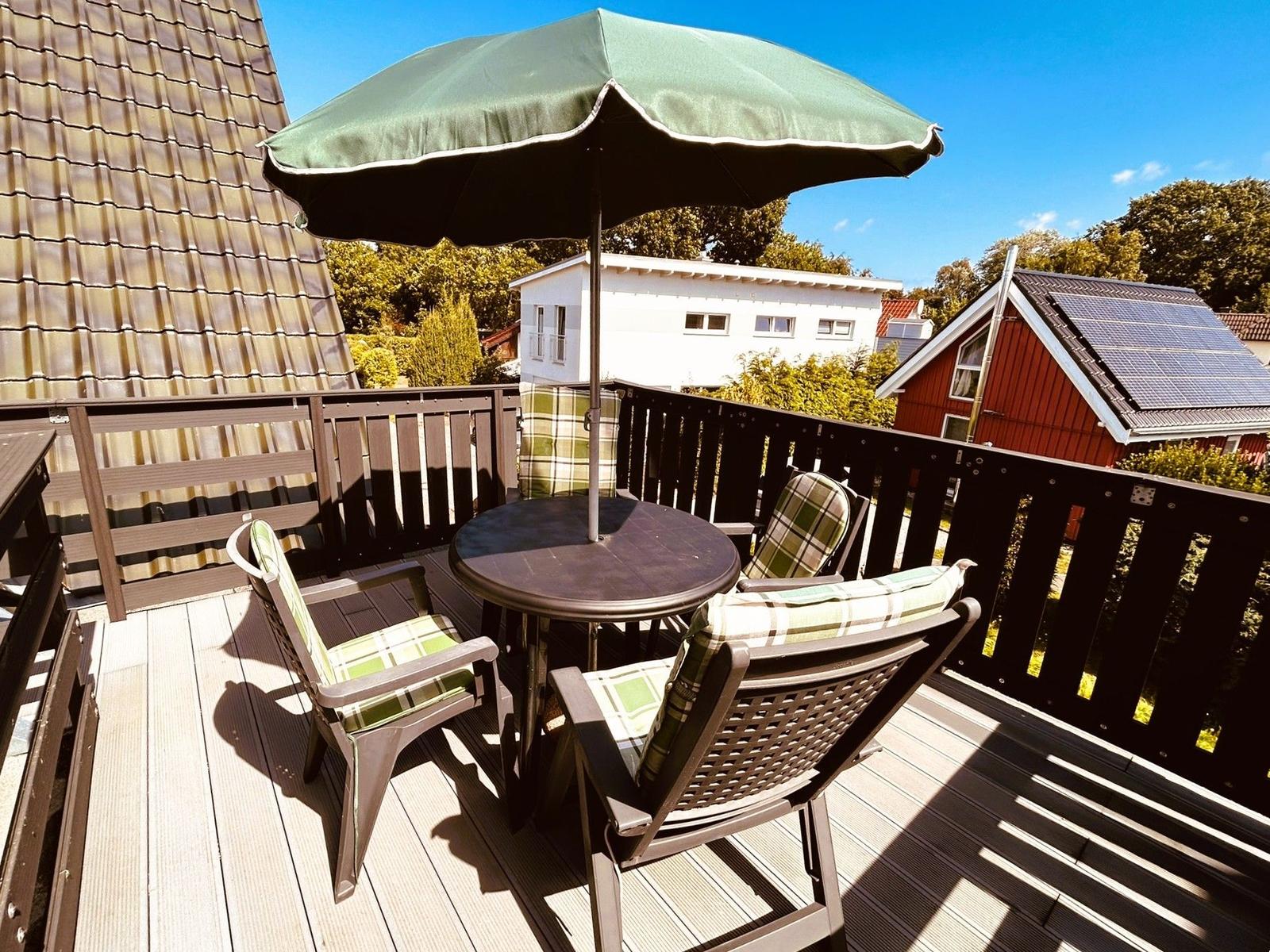 Terrasse mit Tisch, Stühlen und Sonnenschutz. Blick auf Nachbarhäuser und Bäume.