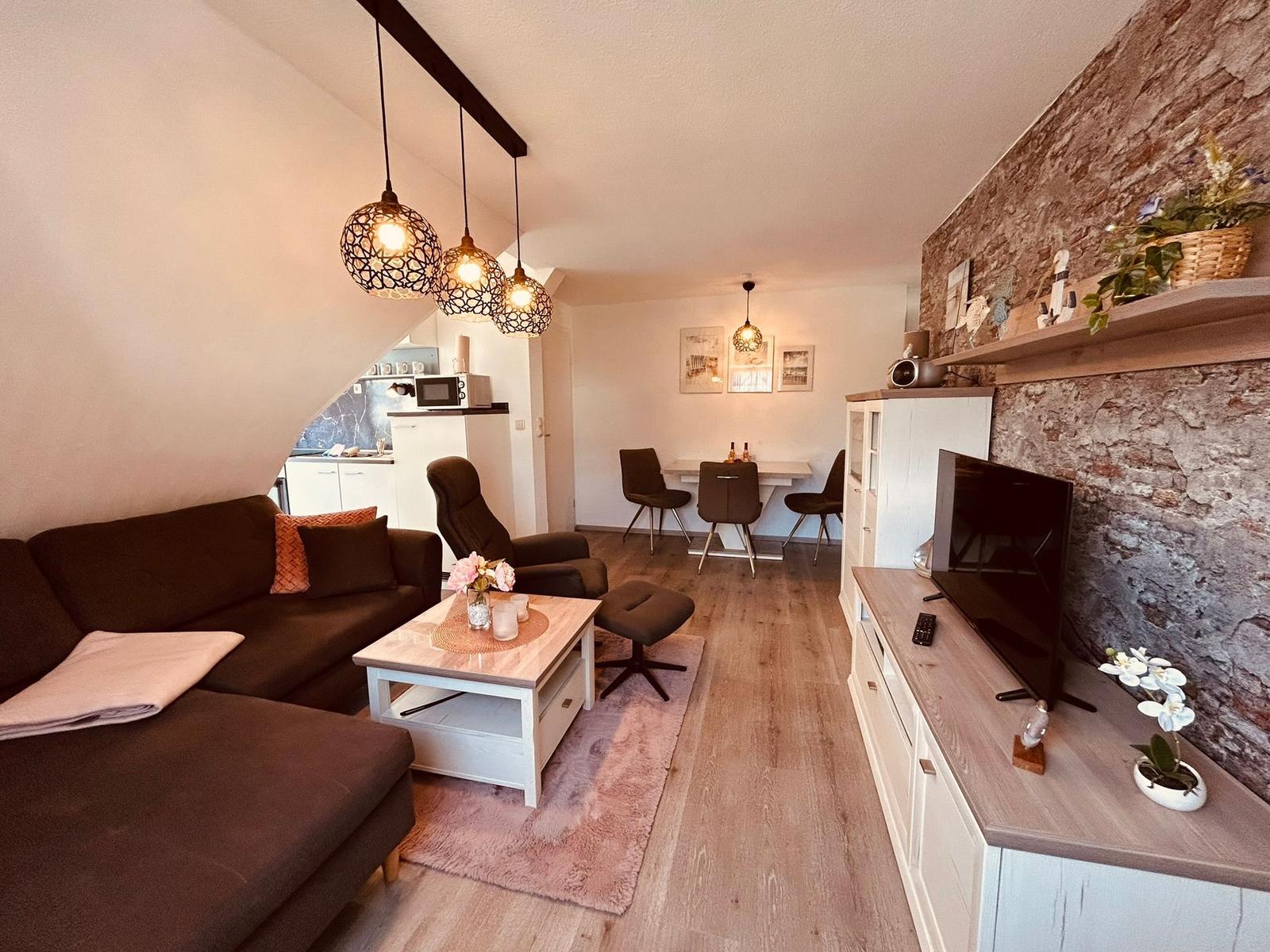 Wohn- und Essbereich mit Sofa, TV und Steinwand. Essplatz mit Tisch und Stühlen.