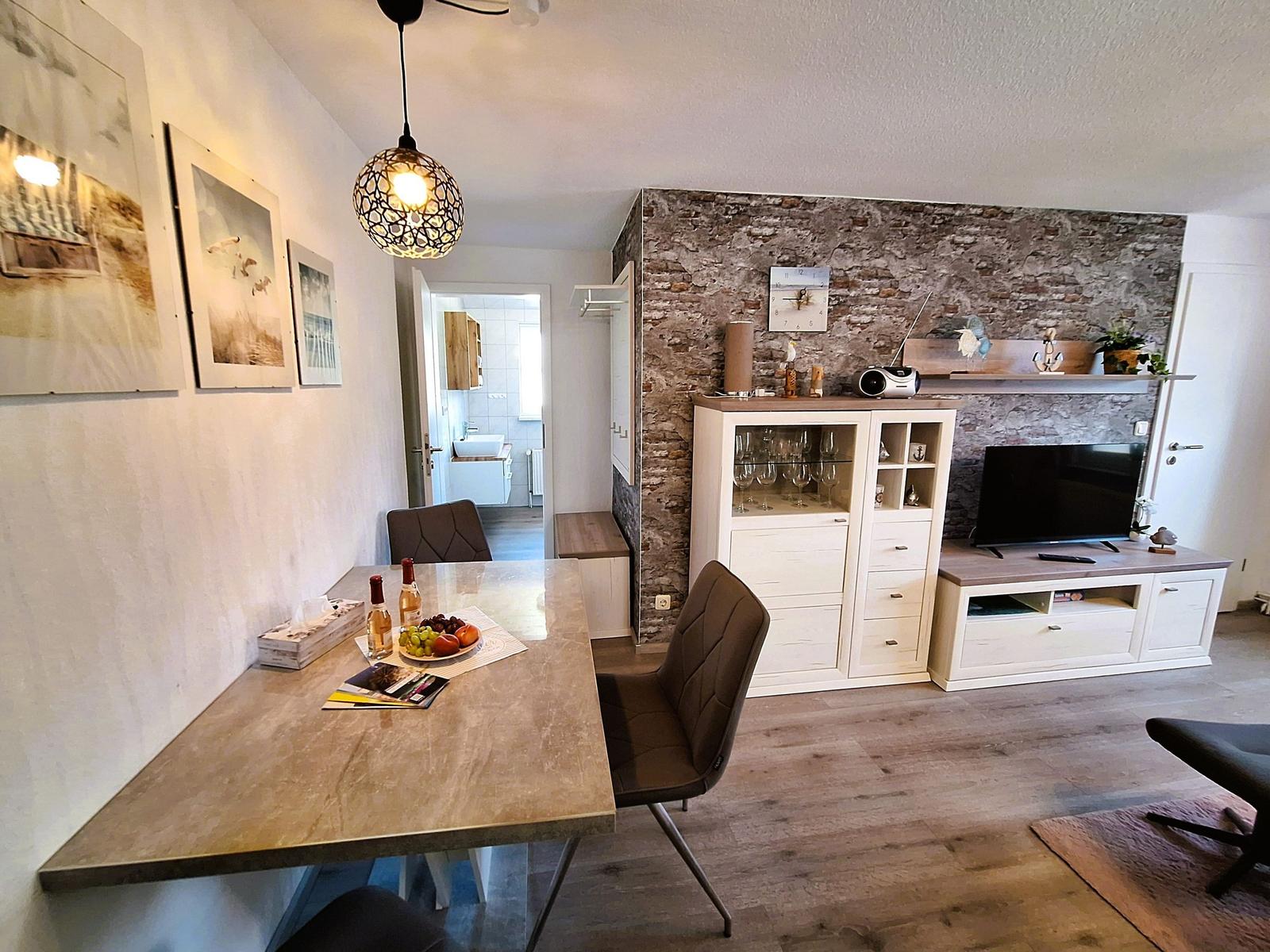 Essbereich mit Tisch und Stühlen. Wohnbereich mit Fernseher und Stehlampe.