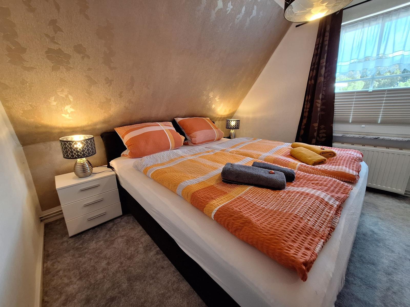 Schlafzimmer mit Doppelbett, Nachttisch und Fenster.