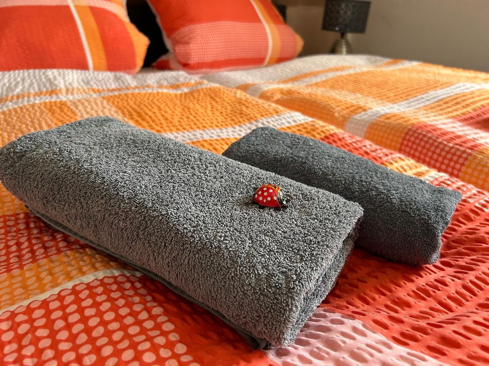 Zwei graue Handtücher liegen auf einem Bett mit bunten Kissen und Bettwäsche.