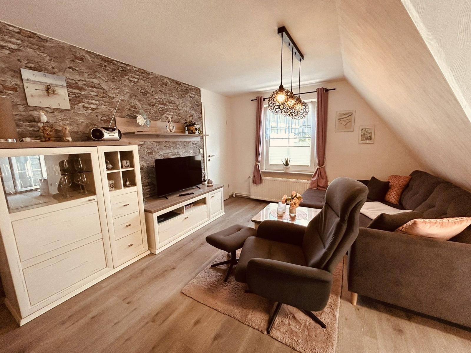 Wohnzimmer mit Sofa, Sessel, TV und Steinwand