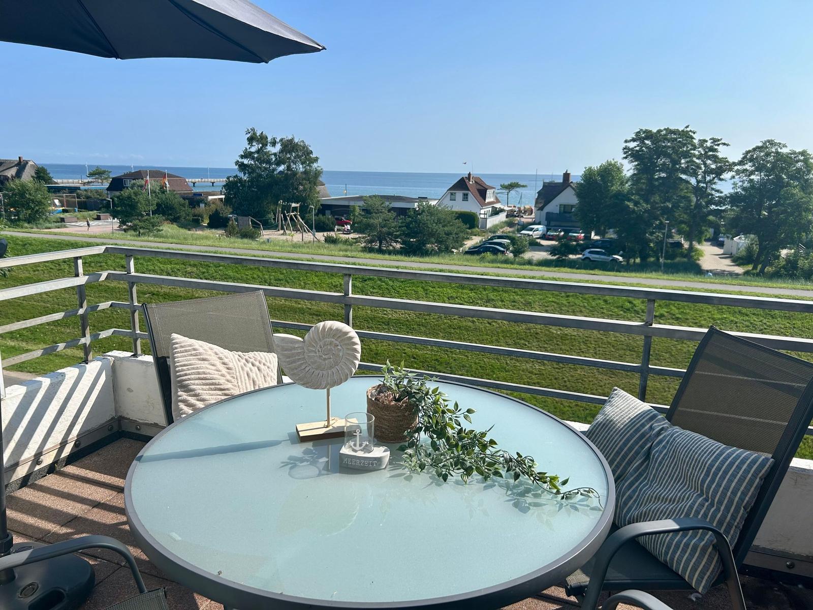 Terrasse mit Tisch und Stühlen. Blick auf Grünfläche und Meer.