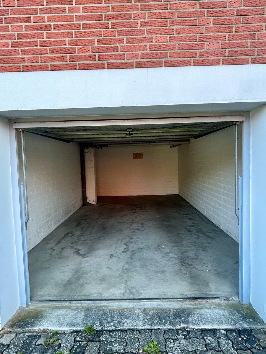 Garage mit Betonboden und weißen Wänden, rote Ziegelwand darüber.