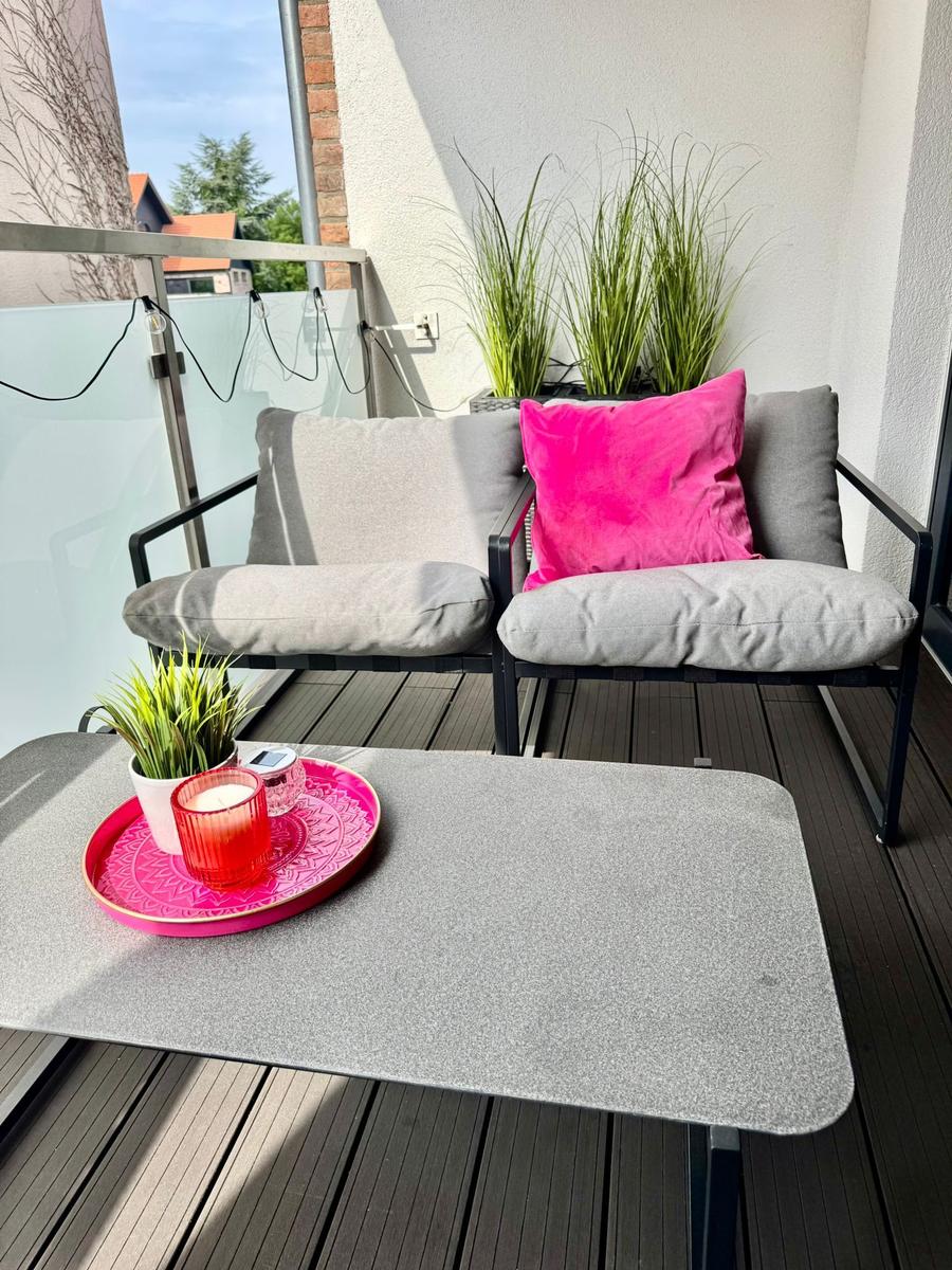 Terrasse mit zwei Sitzgelegenheiten, Tisch und Pflanzen.